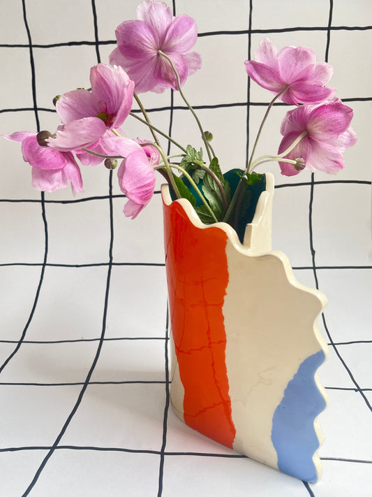 Colorful vase with pink flowers against a black and white grid patterned wall.
